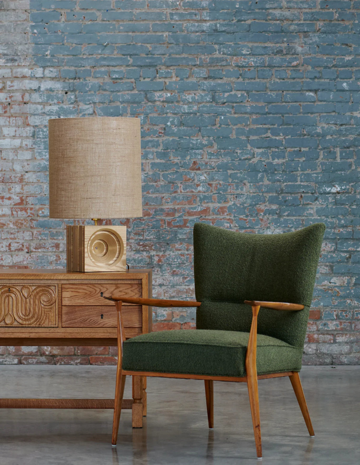 Prague desk lamp on a wooden cabinet beside a green armchair