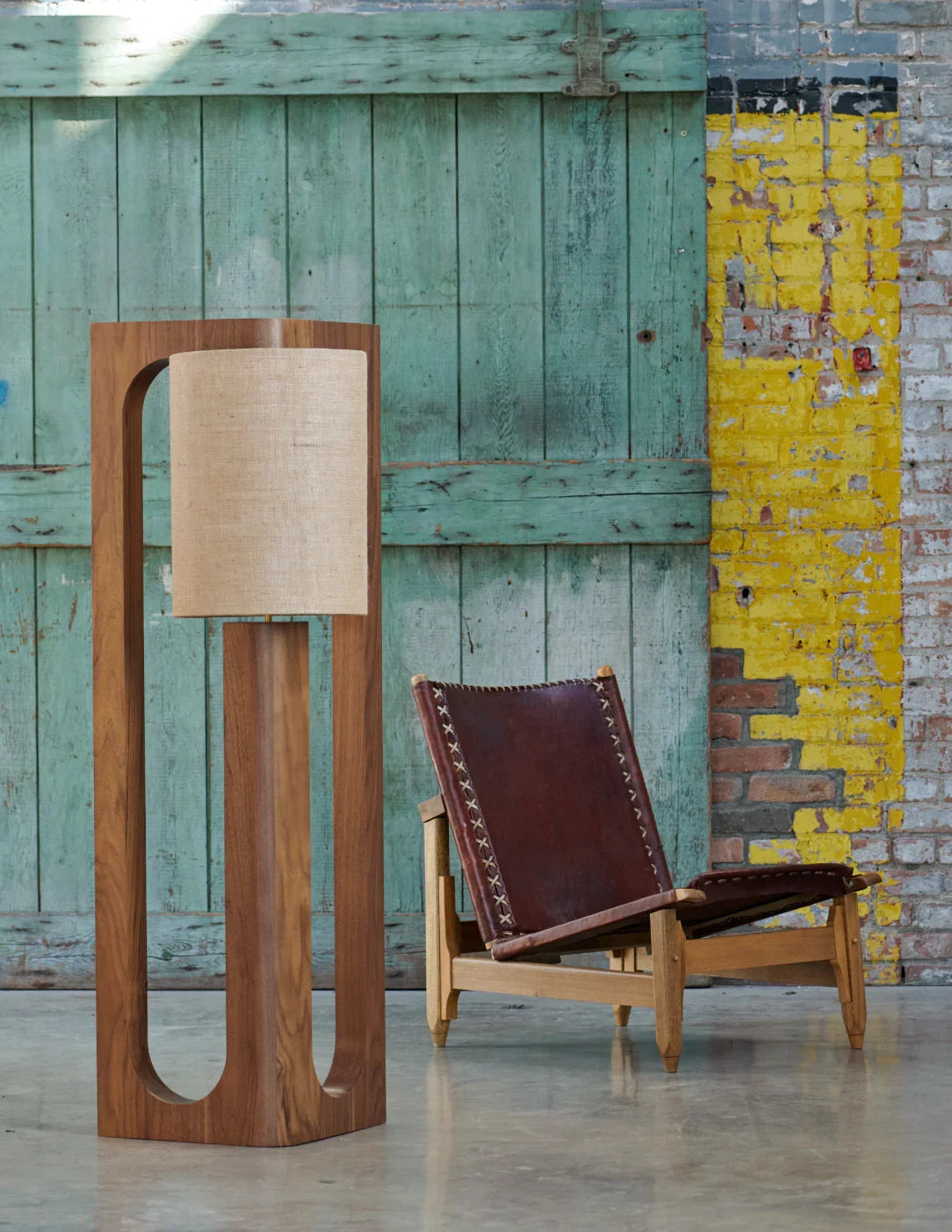 Prague floor lamp in walnut beside a leather sling chair